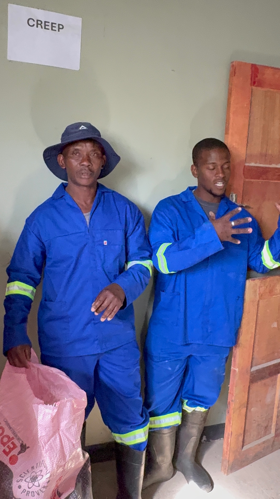 Two Mdaks Farming staff members in blue overalls by the creep room