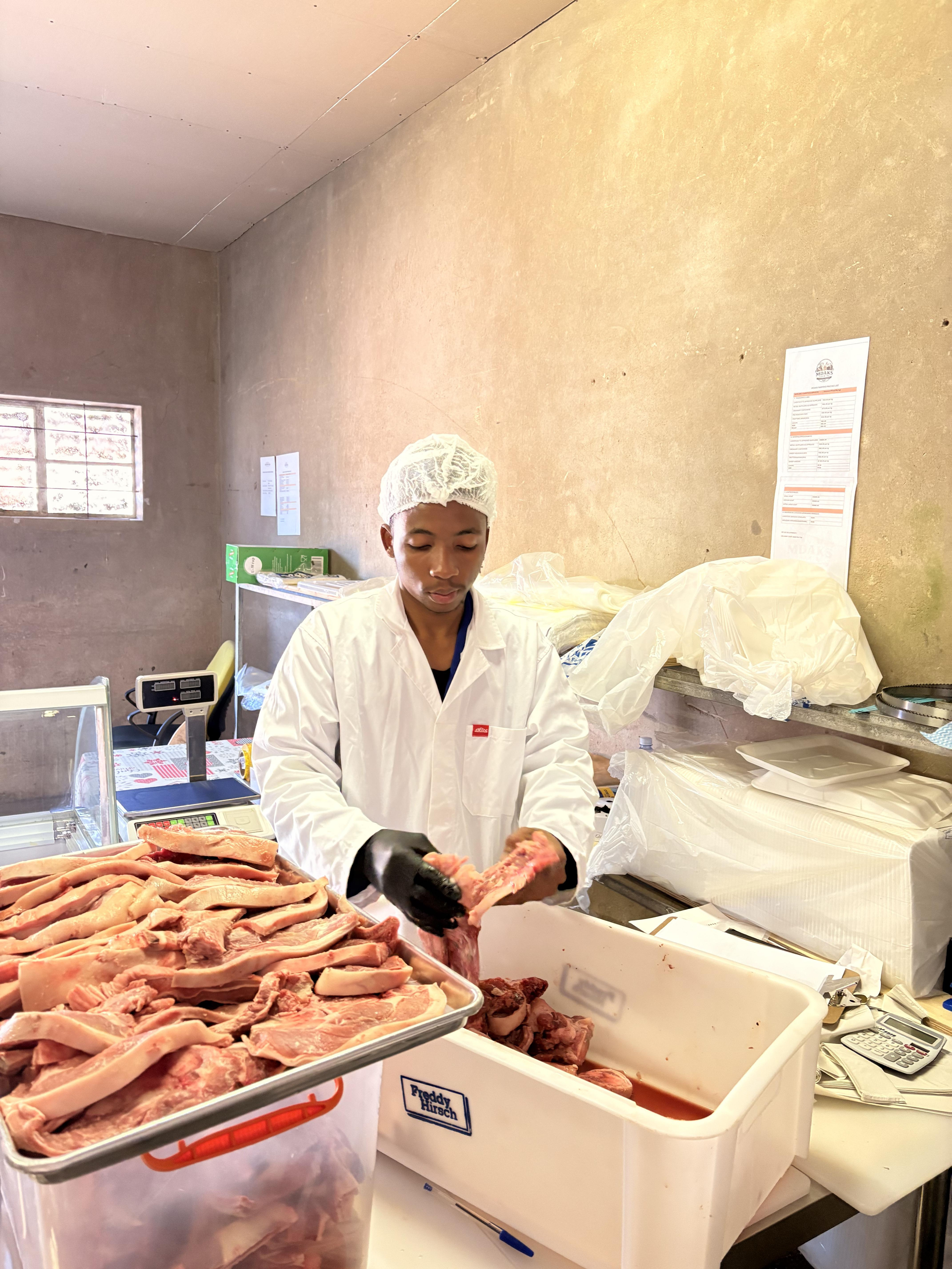 Young Mdaks Farming butcher preparing fresh pork cuts at the processing bench
