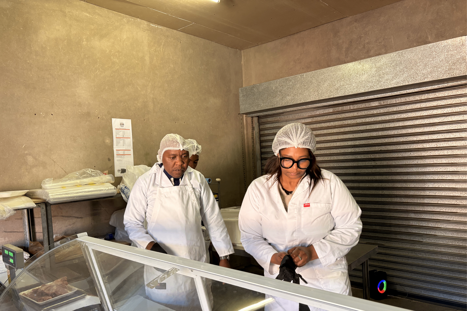 Mdaks Farming owner and manager in white coats and hairnets behind the butchery display counter