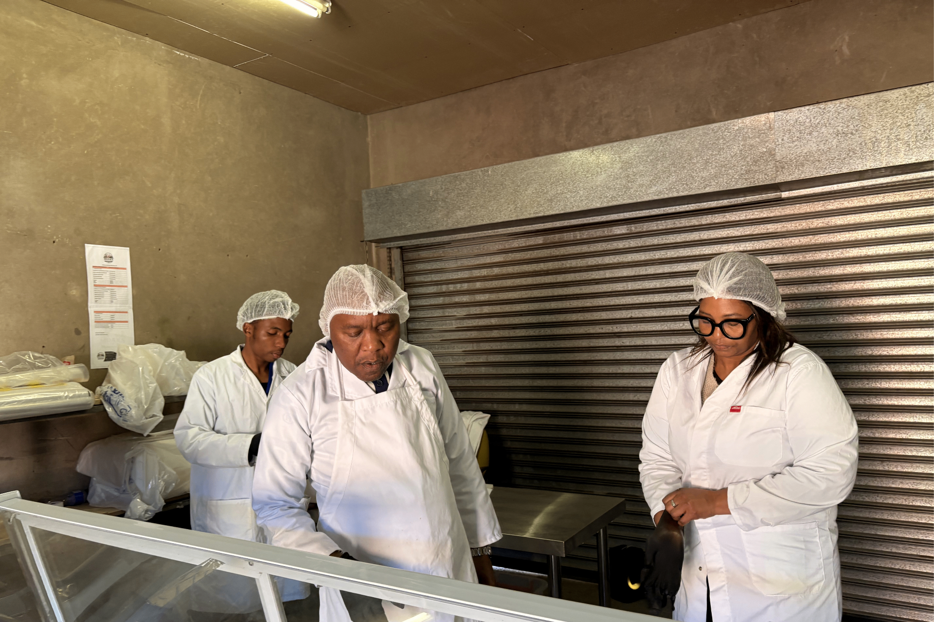 Three Mdaks Farming staff in white coats and hairnets preparing meat in the butchery back room